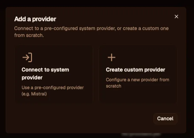 The "Add a provider" dialog with two large options side by side: "Connect to system provider — Use a pre-configured provider (e.g. Mistral)," and "Create custom provider — Configure a new provider from scratch." A Cancel button sits at the bottom.